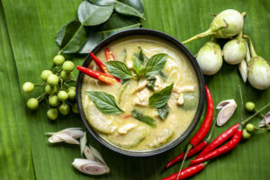 Chicken green curry Thai food on soup bowl with ingredient vegetable herbs and spices pepper chili on banana leaf background, Traditional green curry chicken cuisine asian food.
