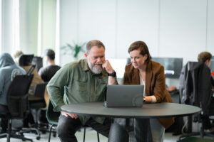 Tony Gorschek och Darja Smite sitter bredvid varandra vid ett bord och tittar leendes på en laptop och pratar om mjukvaruutveckling