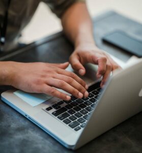 Person som sitter vid en laptop, endast händerna, och datorn syns. Hen jobbar på projekt